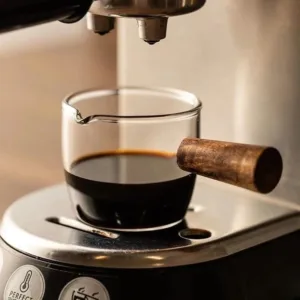 Pichet doseur en verre avec poignée en bois versant du lait dans un café