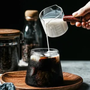 Pichet doseur en verre avec poignée en bois versant du lait dans un café