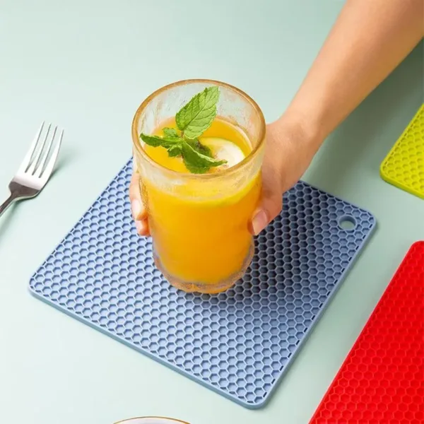 Dessous de plat isolant en silicone, de différentes couleurs, utilisé pour manipuler une casserole chaude sur un plan de travail en cuisine.