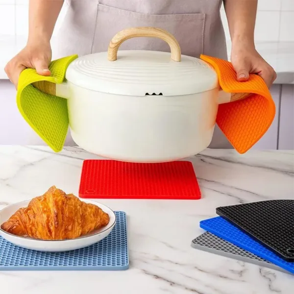 Dessous de plat isolant en silicone, de différentes couleurs, utilisé pour manipuler une casserole chaude sur un plan de travail en cuisine.