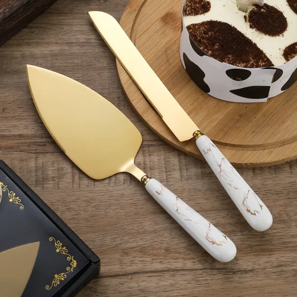 Ensemble de service à gâteau en acier inoxydable doré avec manche noir marbré, comprenant un couteau et une pelle, disposé sur une table élégante.