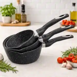 Set de casseroles en granite noir moucheté Olina empilées sur un plan de travail avec ingrédients