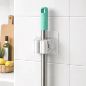 Support mural balai autocollant transparent tenant un manche de balai sur carrelage blanc dans une cuisine au Maroc