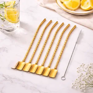 Set de pailles cuillères en inox doré réutilisables avec goupillon de nettoyage posé sur une table en marbre