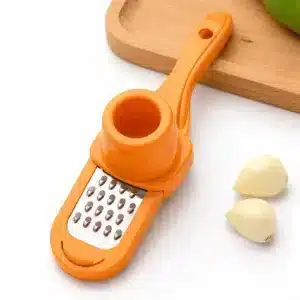 Râpe Ail Manuelle verte avec poussoir râpant l’ail sur une assiette