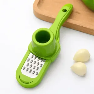 Râpe Ail Manuelle verte avec poussoir râpant l’ail sur une assiette