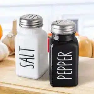 Set salière et poivrière noire en verre sur une planche à découper.